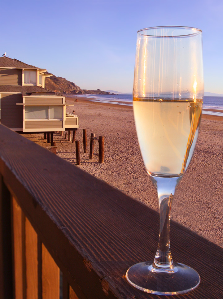 a glass of wine set on a railing overlooking a beach with a house in the background