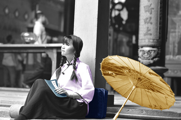 A young woman sitting near an umbrella, holding a thin book